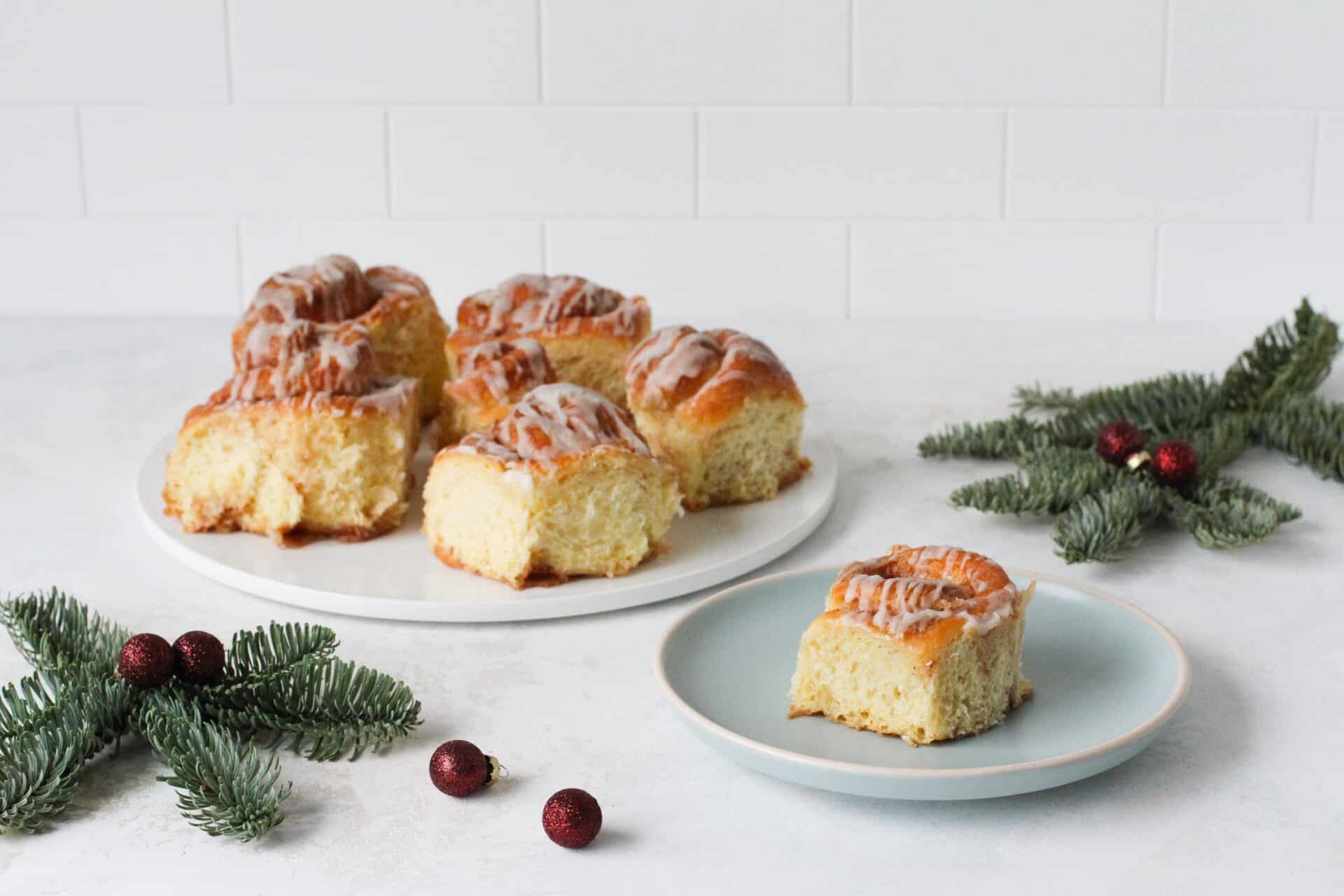 Festive eggnog cinnamon rolls with a boozy glaze, arranged on a white marble plate and a blue small plate to serve one roll.