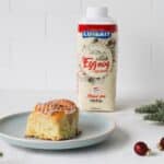 Festive eggnog cinnamon roll with a boozy glaze, arranged on small plate to serve the roll as well as the eggnog carton.