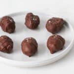 Chocolate Almond Butter Dates are sitting on a white marble platter. The dates are filled with almond butter, and dipped into dark chocolate.