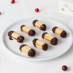 Marzipanstangen cookies with golden dough and tart cherry jam, dipped in dark chocolate, arranged with holiday decorations.