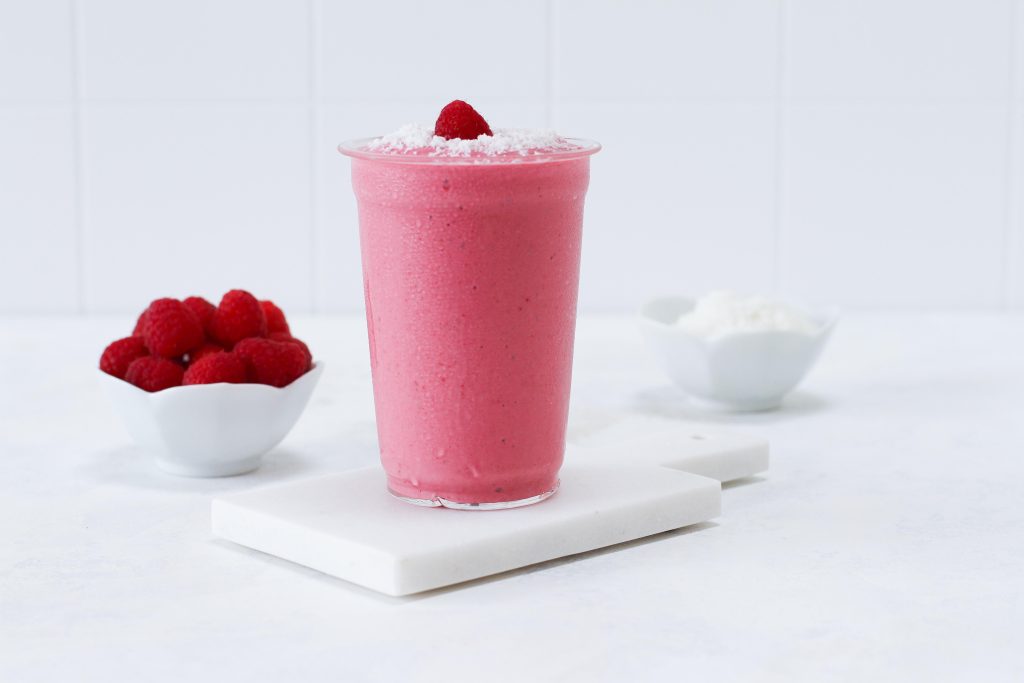 Glass with raspberry coconut smoothie topped with a fresh berry and coconut flakes